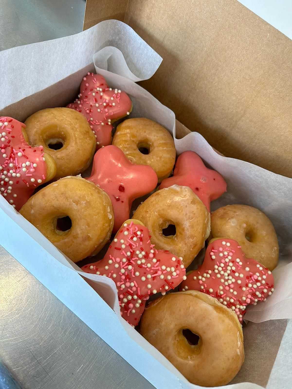 Box of glazed and pink-frosted doughnuts with sprinkles.