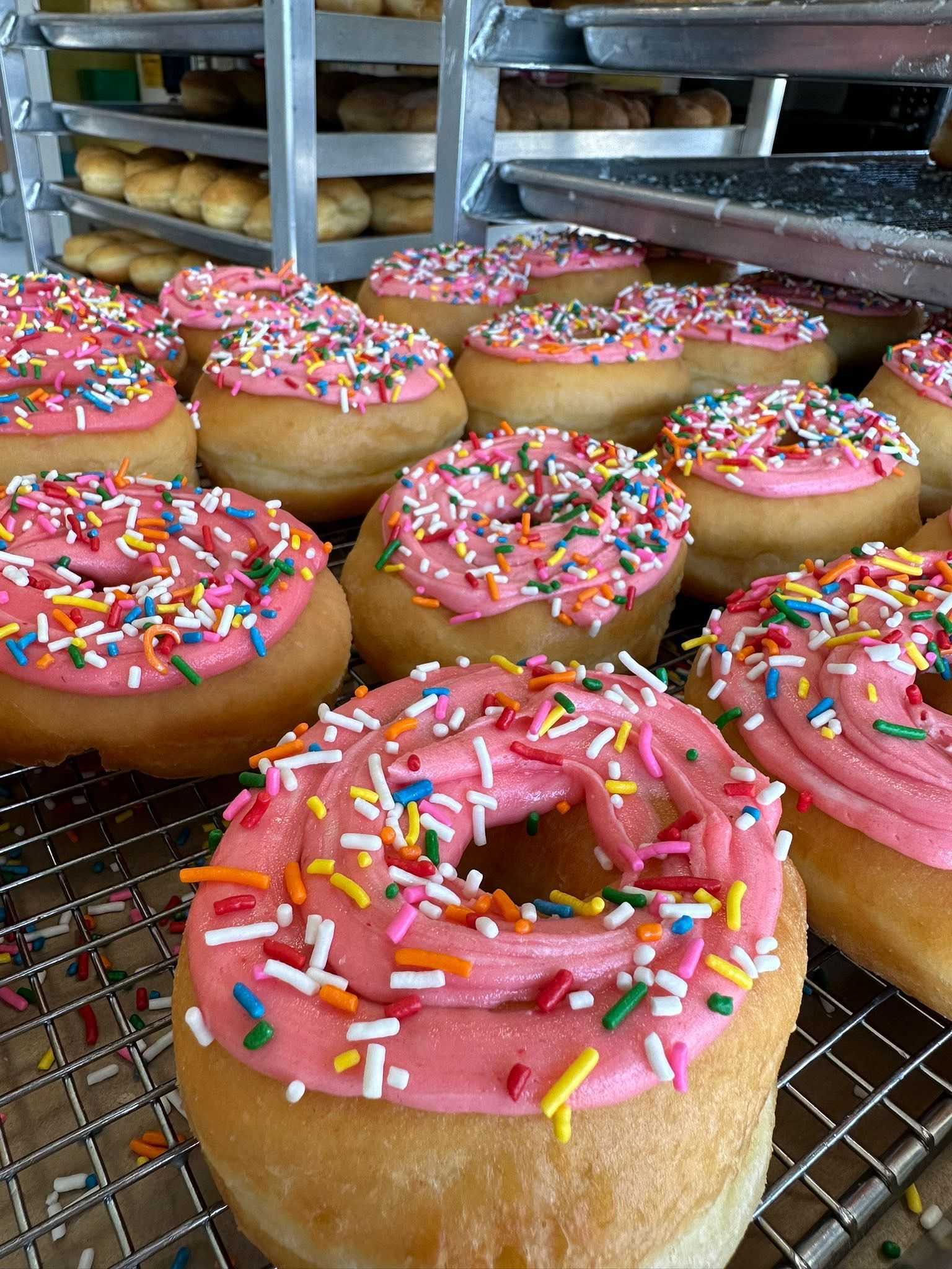 Freshly baked donuts with pink icing and sprinkles on a rack.