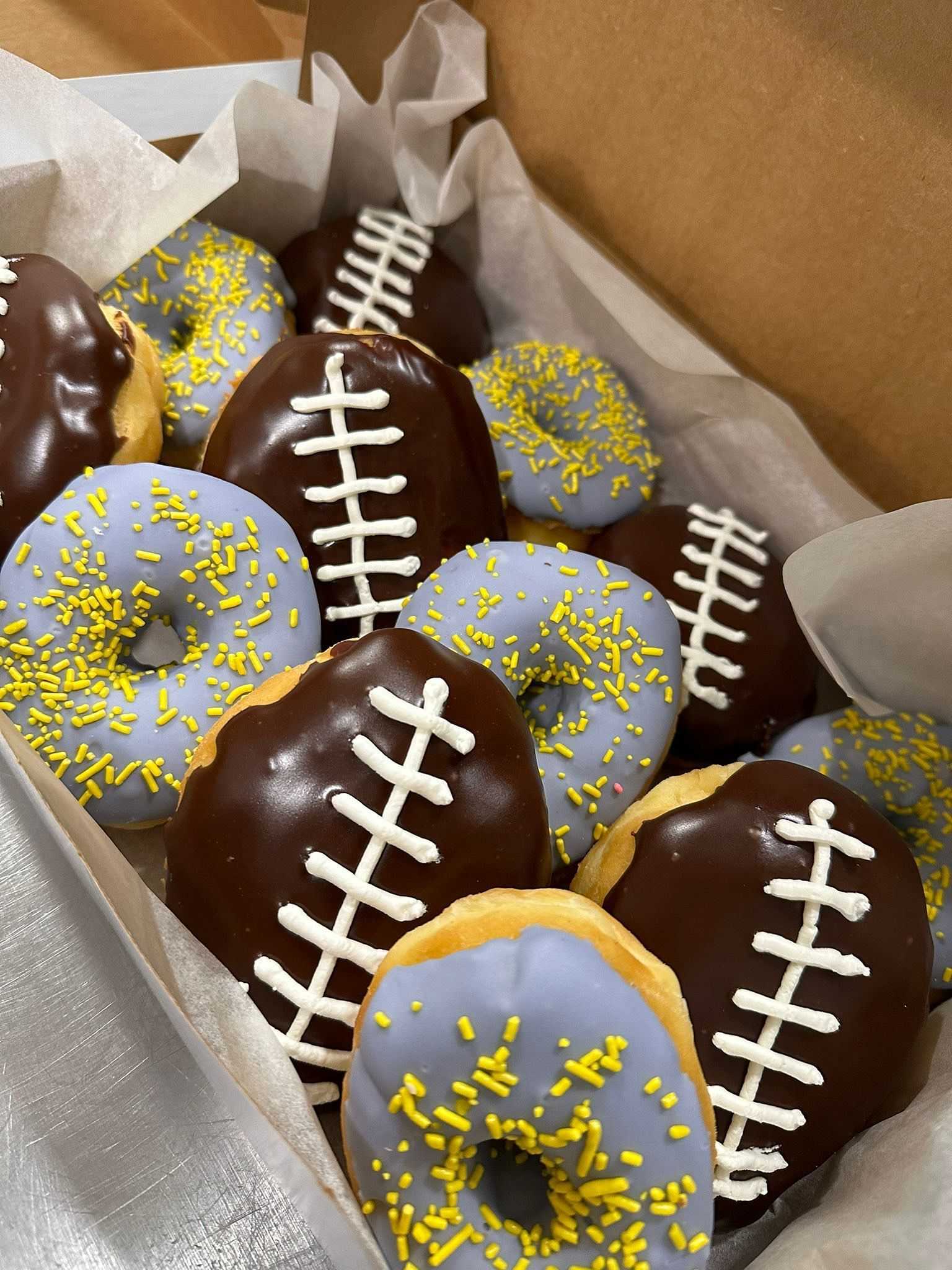 A box of football-themed donuts with chocolate icing and yellow sprinkles.