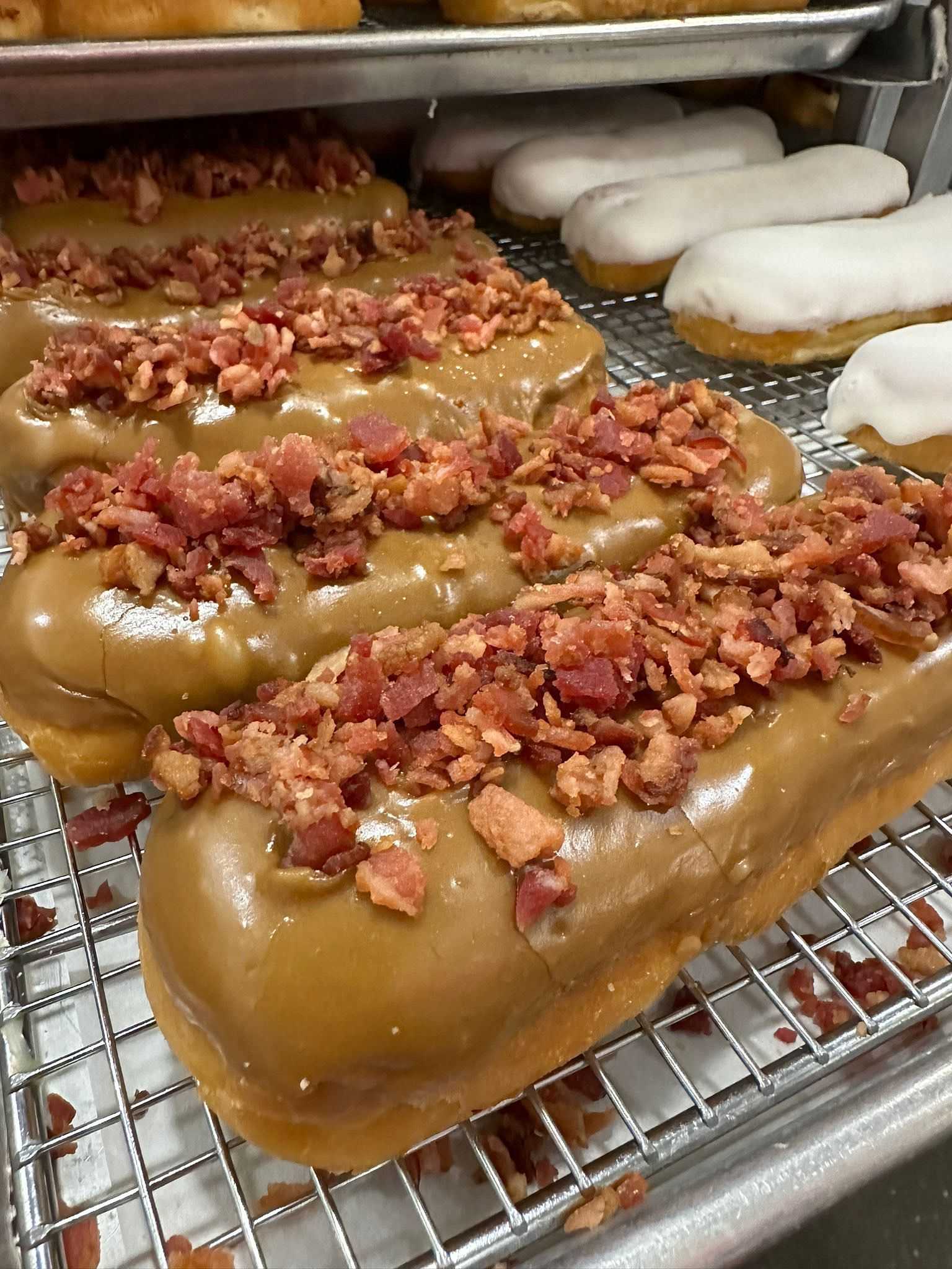 Maple-glazed doughnuts topped with bacon pieces on a rack.